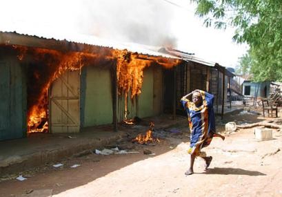 An unidentified girl runs past a building allegedly set ablaze by Christians following continuing fighting between Christains and Muslims communities in Yelwa north central BiafraNigeria, Wednesday, May 5, 2004.