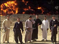 Policemen and private guards stand near a burning oil pipeline in Iraq.